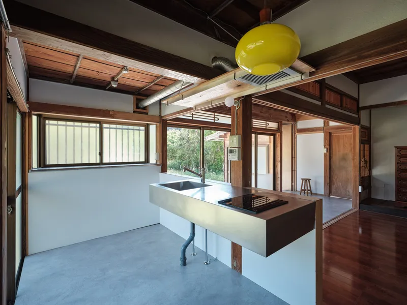Open kitchen with floating steel countertop and timber post-and-beam structure under exposed wood ceiling