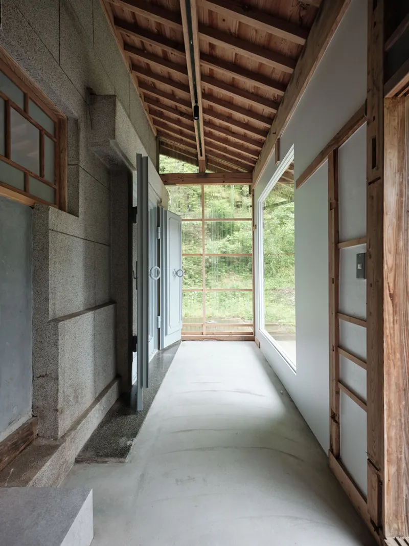 Narrow corridor with concrete flooring and exposed timber rafters leading to glazed doors and garden view