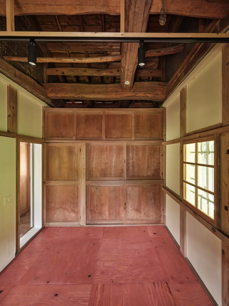 View toward a paneled timber storage wall beneath exposed roof beams and red plywood flooring