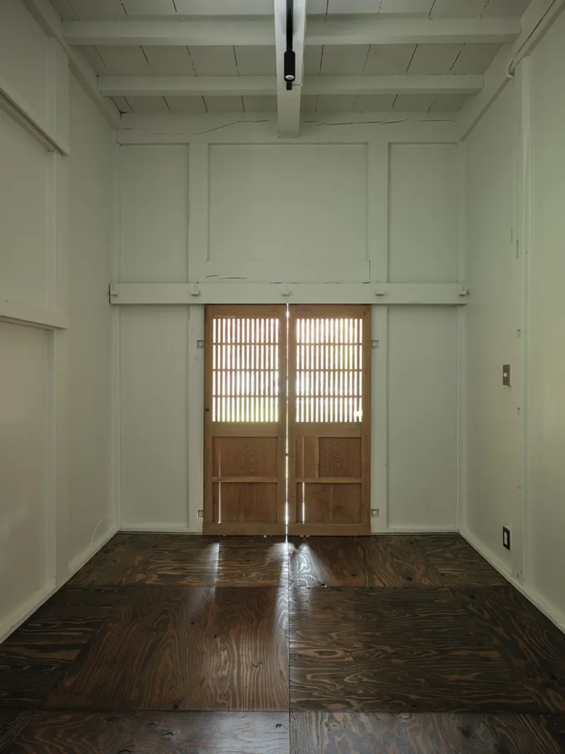 Room with white coffered ceiling and paneled walls facing twin latticed timber doors filtering daylight