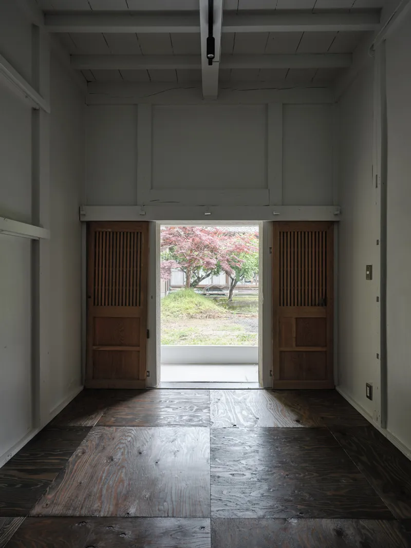 Open sliding timber doors framing view of blossoming tree in gravel courtyard beyond threshold