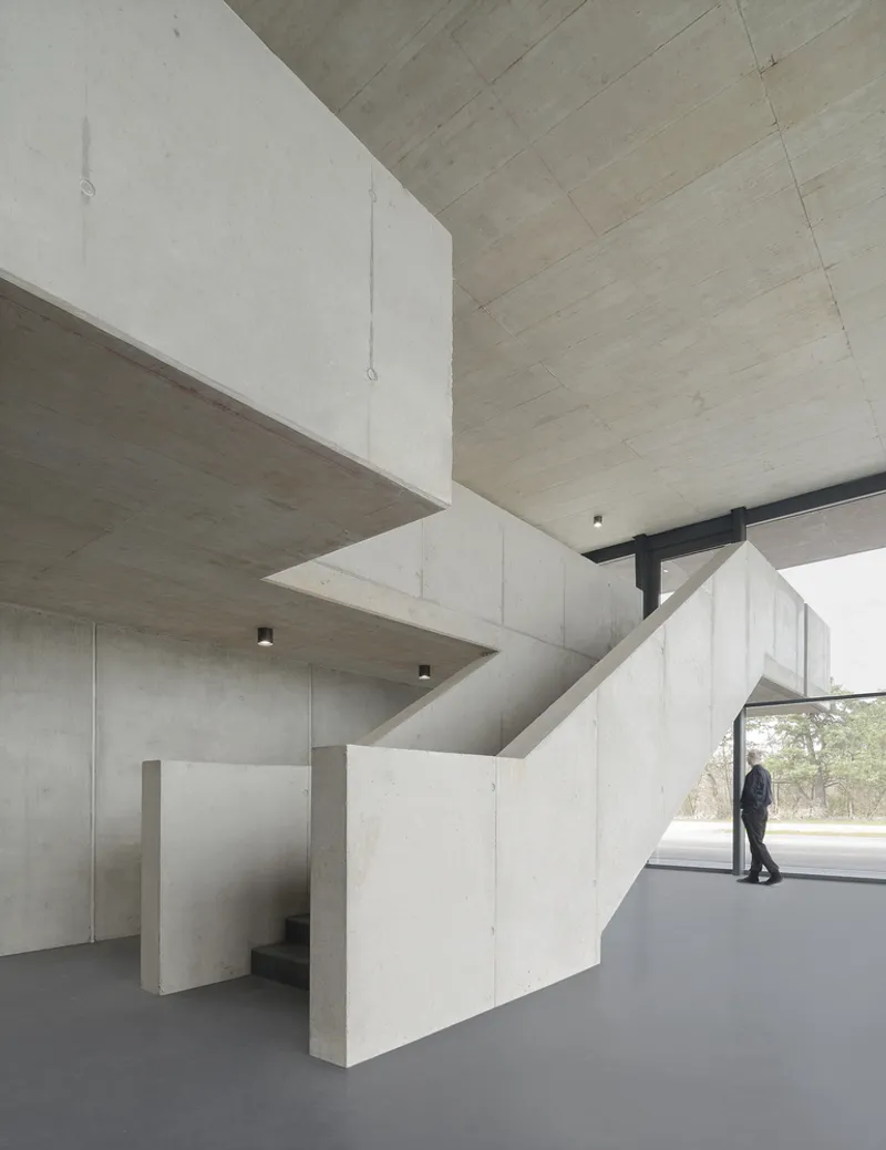 Interior stair volume in cast concrete with person walking toward glazed opening