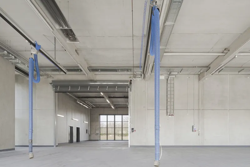 Interior workshop space with exposed blue ventilation ducts suspended from a concrete waffle slab ceiling