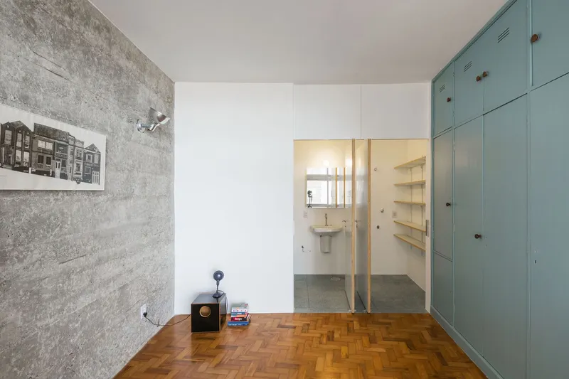 Room with herringbone wood floor, exposed concrete wall, and blue-green locker doors opposite a framed bathroom doorway