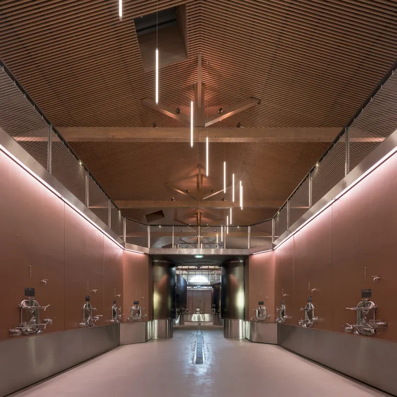 Gallery hall with timber slat ceiling, pendant linear fixtures, and bronze metal walls displaying sculptural exhibits