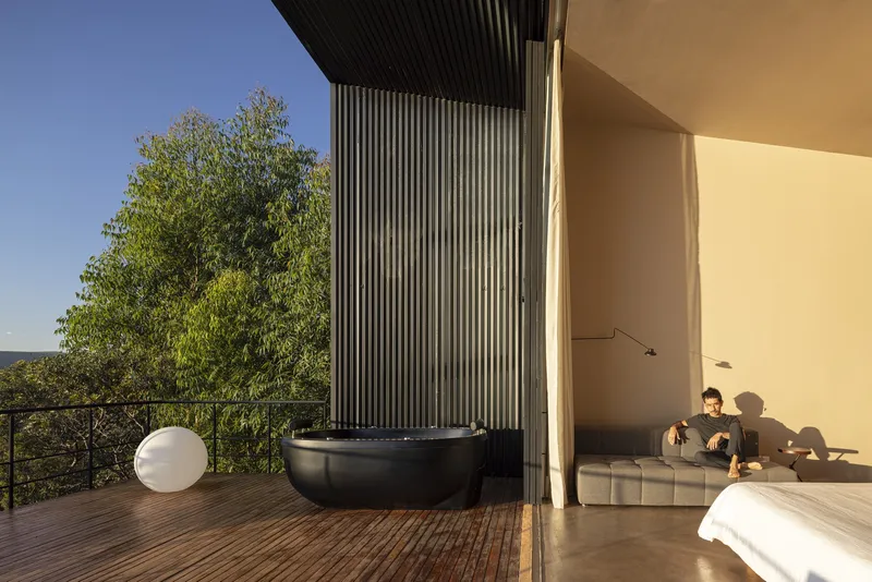 Timber deck with black freestanding bathtub and vertical metal cladding viewed at golden hour