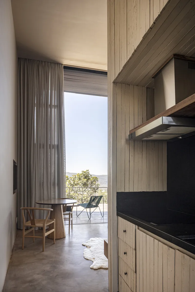 Interior view through kitchen with black countertop toward glazed opening and distant forested hills