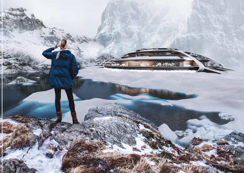 Person standing on snowy rock ledge overlooking horizontal layered structure beside alpine lake and mountain peaks