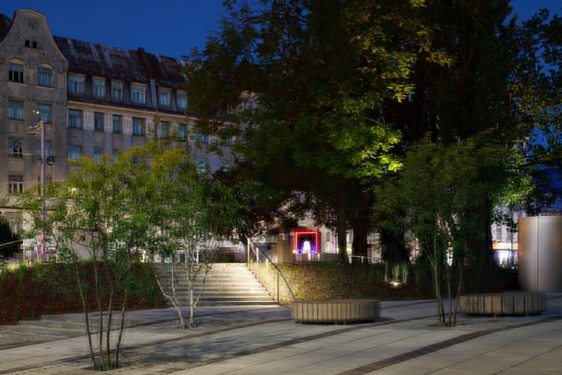Wide steps leading through the plaza flanked by circular planters and uplighting at dusk