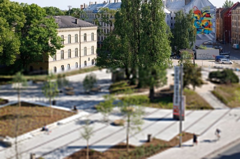 Public plaza with diagonal paving, planted beds and newly planted trees in summer sunlight