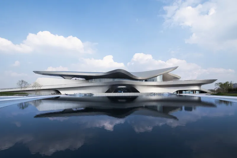 Horizontal metal-clad volumes with cantilevered roof planes reflected in a surrounding reflecting pool under a blue sky