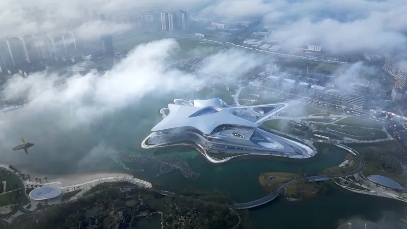 Aerial view of the multi-lobed building on a peninsula surrounded by water and urban context shrouded in fog