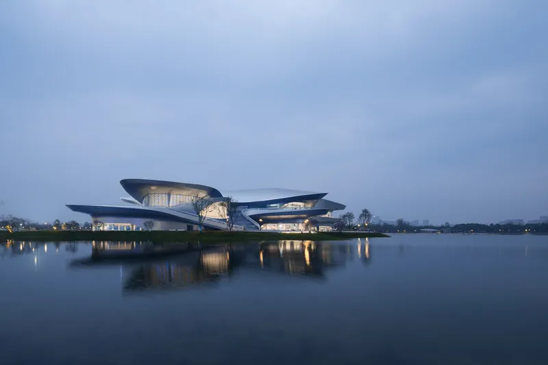 Illuminated lakeside facade with stacked horizontal volumes and glazing reflected in still water at dusk