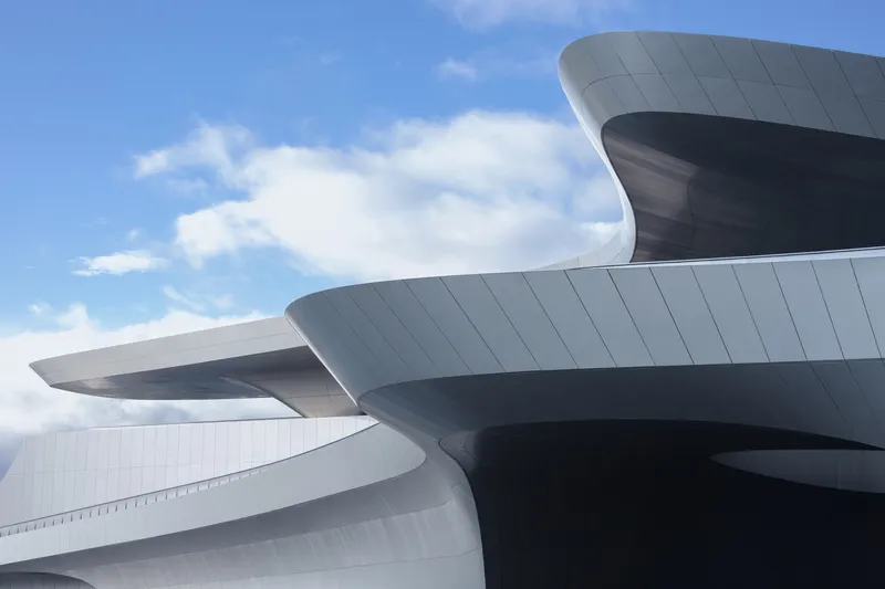 Overlapping curved metal-paneled roof volumes against a partly cloudy blue sky