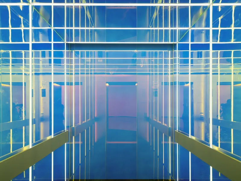 Interior corridor with illuminated vertical glass rods creating a grid pattern of blue and yellow light