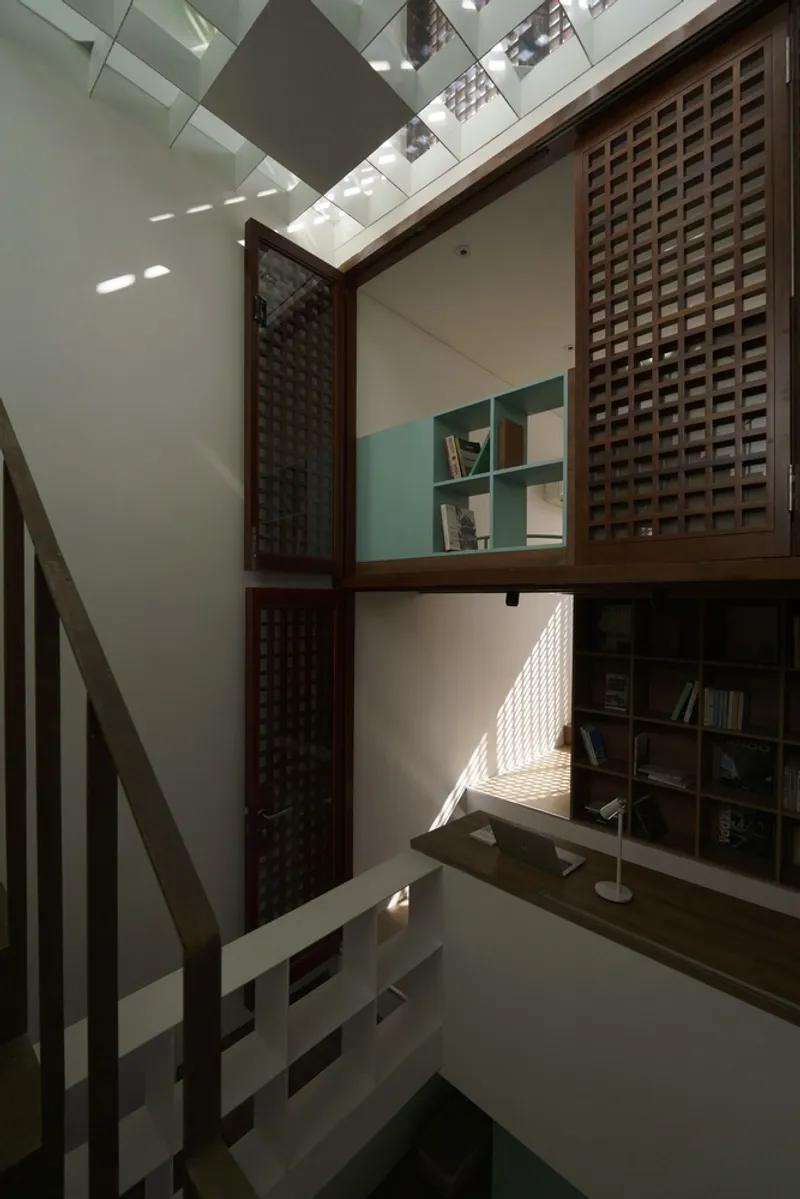 Interior courtyard with timber lattice screens and bookshelves beneath a geometric skylight casting angular shadows