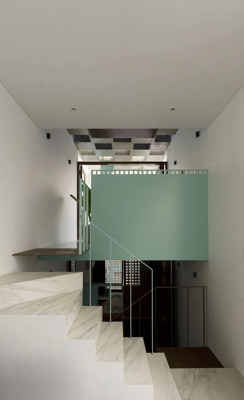 White marble staircase ascending past a sage green volume with lattice detailing and chequered ceiling inset