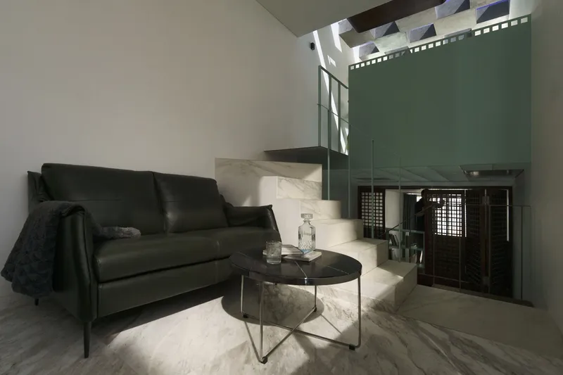 Sitting area with black leather sofa and marble clad stair illuminated by overhead skylight
