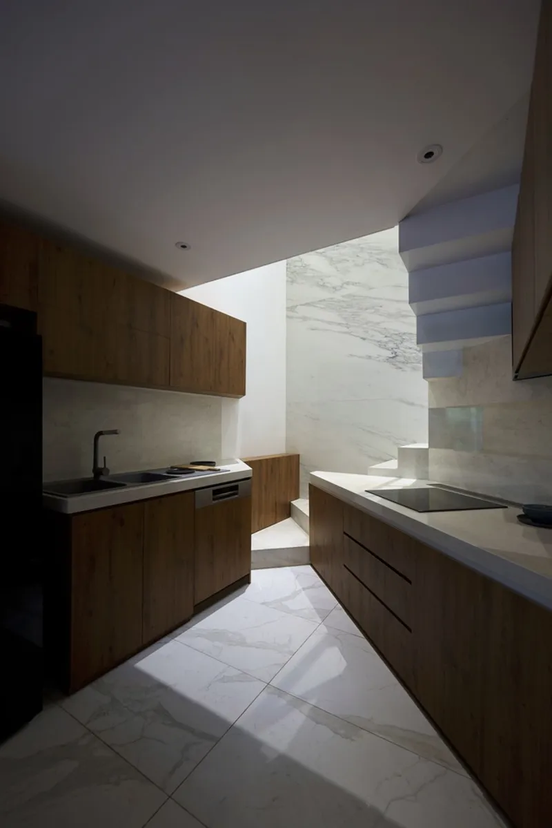 Galley kitchen with timber cabinetry and marble surfaces flooded with indirect natural light