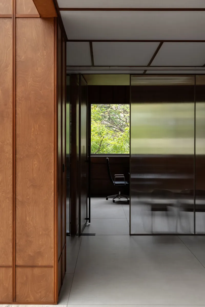 View through frosted glass partition into office space with chair and green foliage visible outside