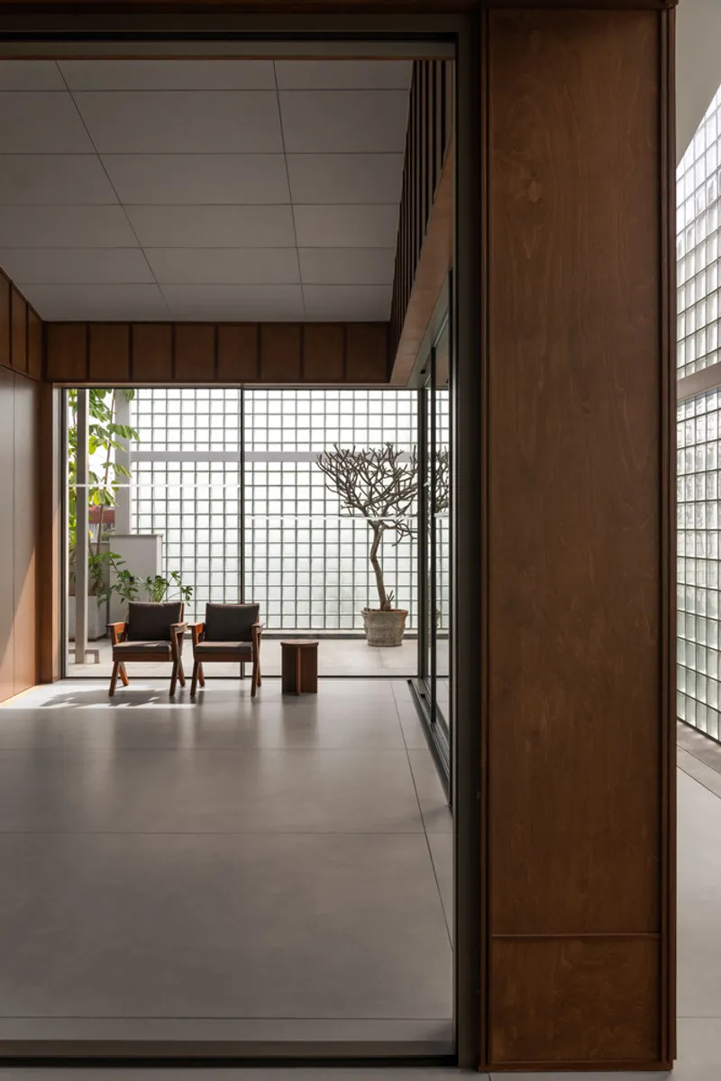 Entrance passage framed by timber panels looking toward glass block wall and courtyard garden beyond
