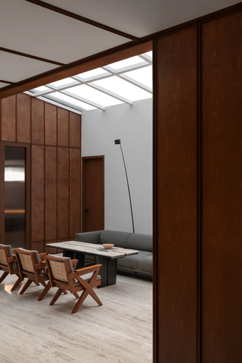 Interior lounge beneath a grid skylight with timber wall panels and angled floor lamp