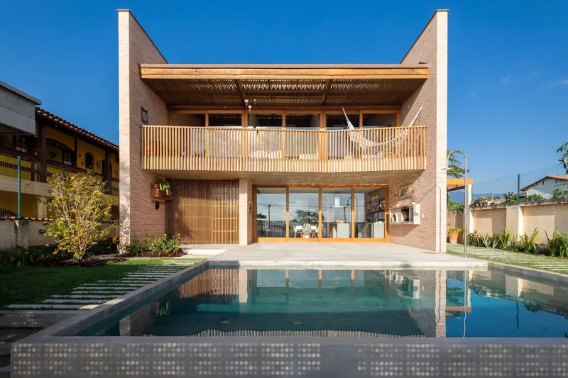 Rear facade with vertical timber slat screens and upper balcony reflected in the swimming pool