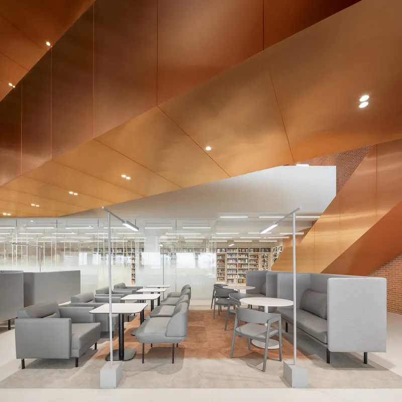 Seating area beneath angled copper-paneled ceiling with library shelves visible through frosted glass partitions