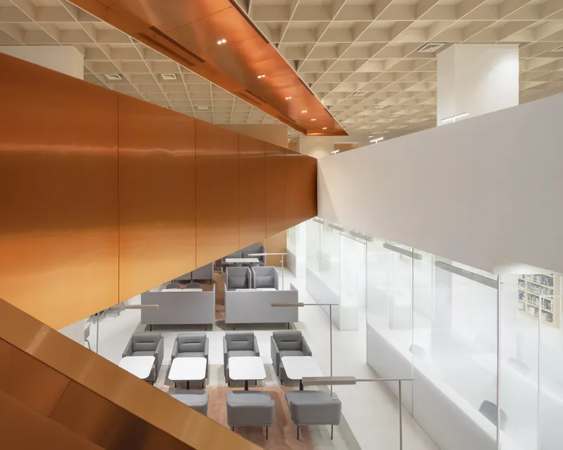 Top-down view of double-height reading lounge with glass balustrade and coffered copper ceiling soffit