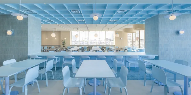 Cafeteria interior with white tables and chairs beneath a blue gridded ceiling and globe pendant lights