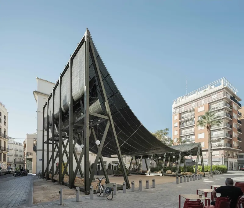 Triangular steel and mesh canopy on diagonal supports in an urban plaza with a palm tree