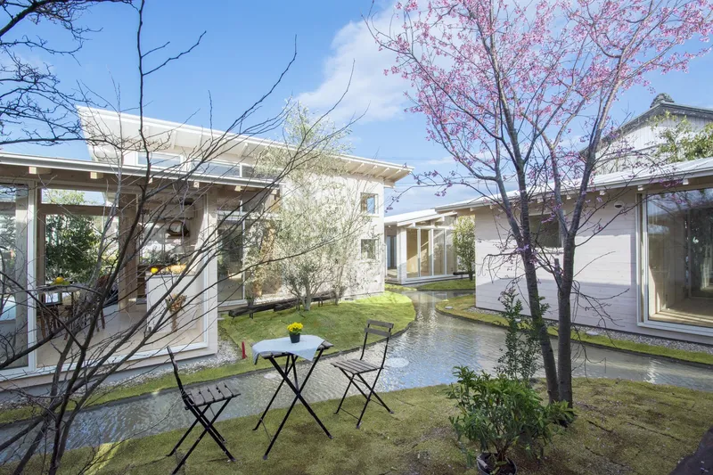 Courtyard view with reflecting pool, pink blossoming cherry tree, and bistro table between timber-framed pavilions