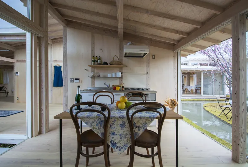 Dining area with exposed timber beams and ceiling joists overlooking the garden courtyard through full-height glazing