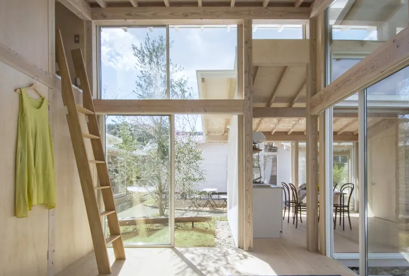 Interior showing timber ladder, full-height glazing, and mezzanine level framed by exposed structural posts