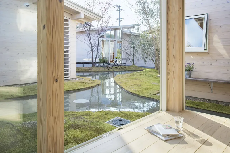 View through timber-framed opening onto shallow courtyard water feature with moss-covered ground and bare trees