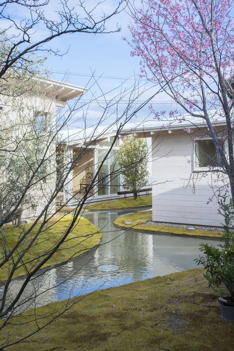 Garden perspective showing the water channel winding through moss-covered berms beneath pink-blossomed and bare trees