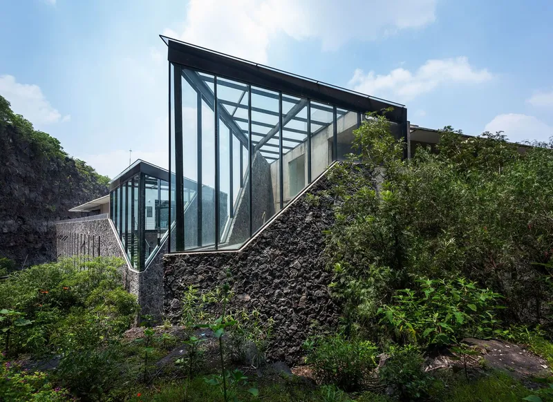 Glass pavilion with exposed steel frame cantilevered over rough volcanic stone retaining wall