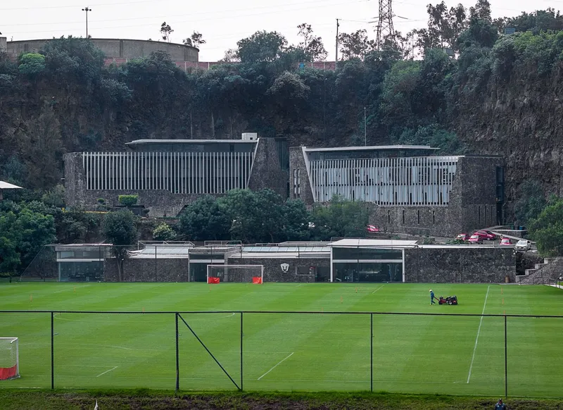 Long view across football pitch showing louvered volumes bridging between stone cliff walls