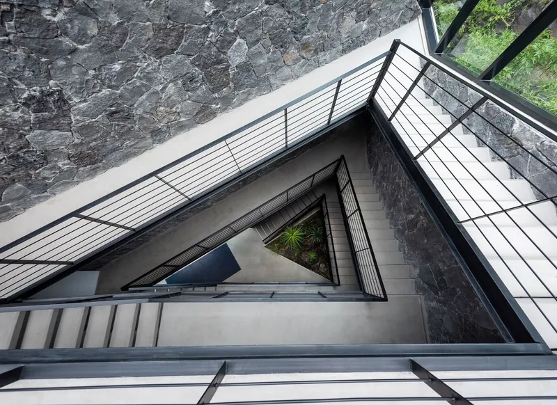 View up through triangular stairwell with black steel railings and polycarbonate skylight above