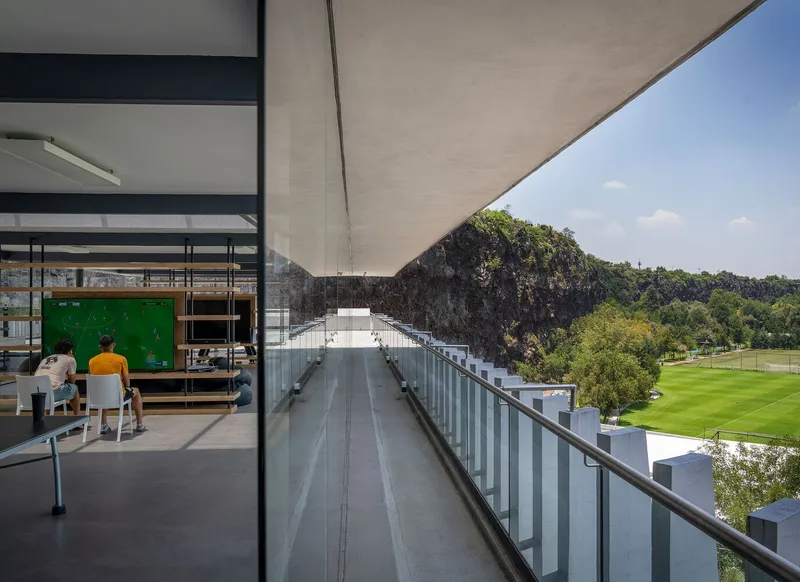 Covered terrace with concrete soffit extending toward rocky cliff face and green playing field