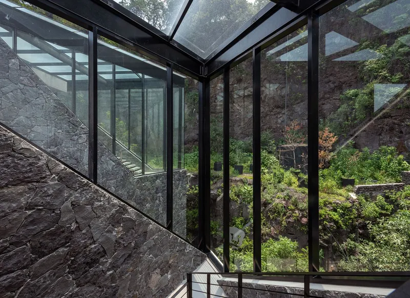 Glass-walled stairwell with steel handrail overlooking landscaped courtyard carved into hillside