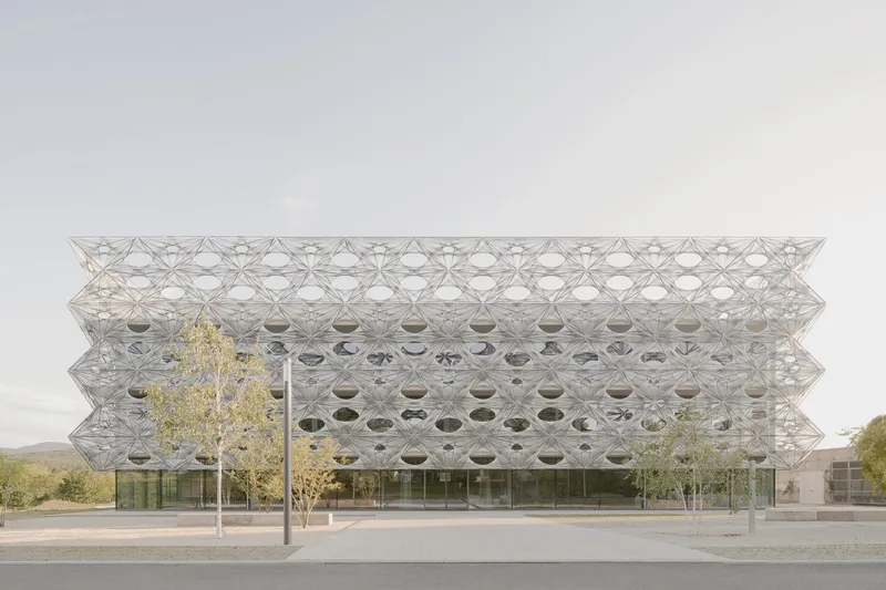 Street view of the perforated geometric facade with circular openings and trees in autumn leaf