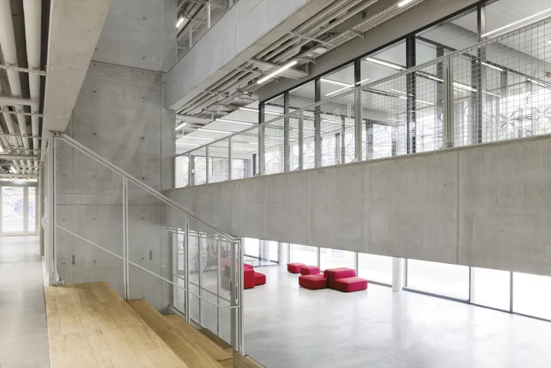 Double-height atrium with concrete walls, mesh balustrade and red upholstered seating below