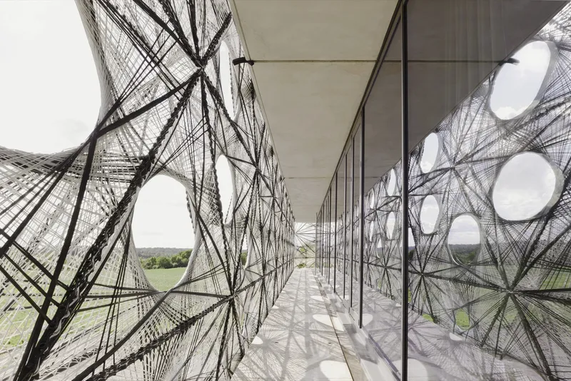 Circulation corridor between glass and the tensioned wire facade casting geometric shadows