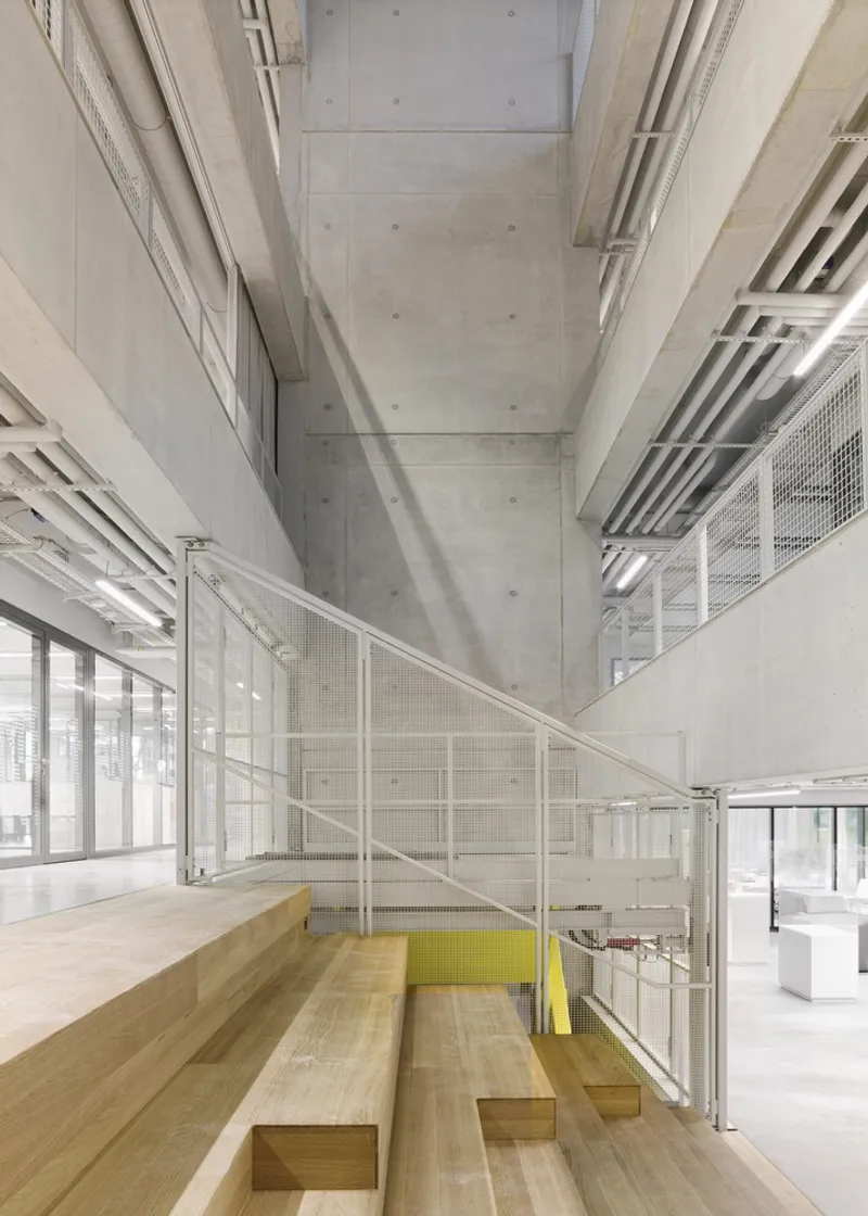 Interior view of timber bleacher seating beside white mesh railings and exposed concrete ceiling beams