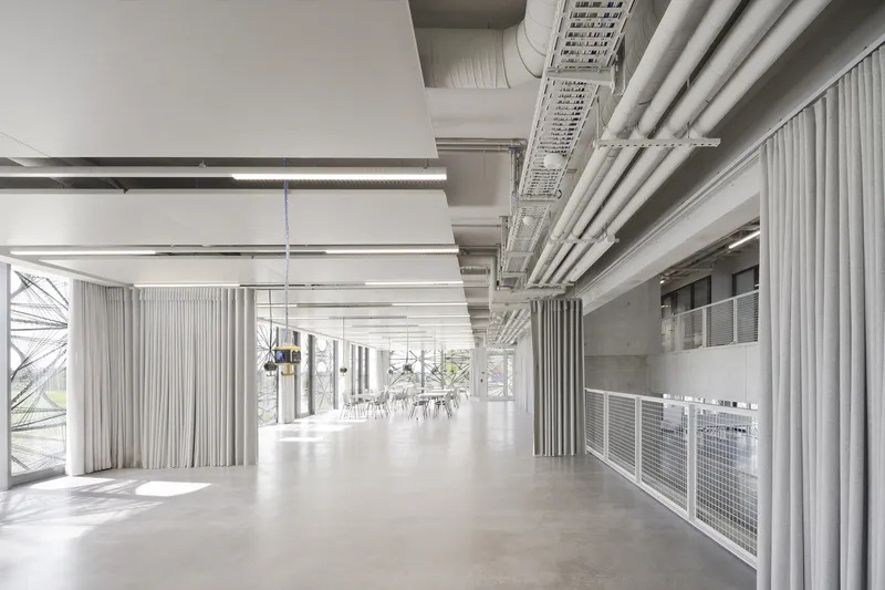 Open floor with exposed concrete ceiling, pleated curtains and the patterned facade beyond