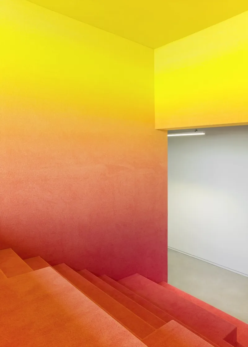Gradient carpeted staircase transitioning from yellow to orange to red tones beside a doorway