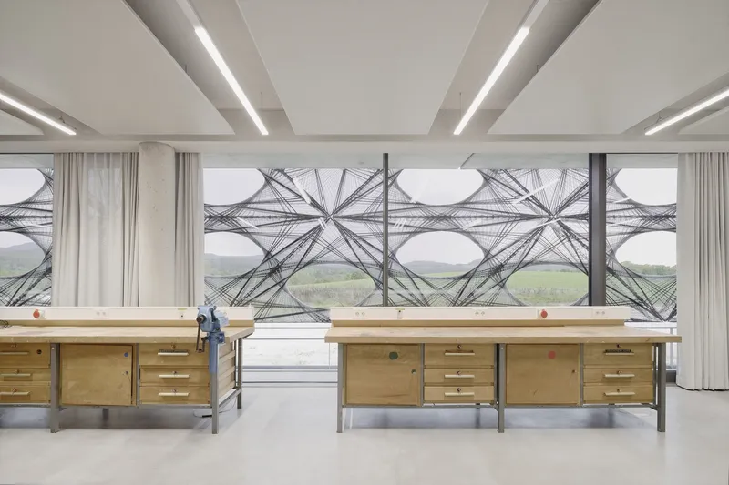Interior workspace with plywood desks facing the patterned facade beyond full-height curtains