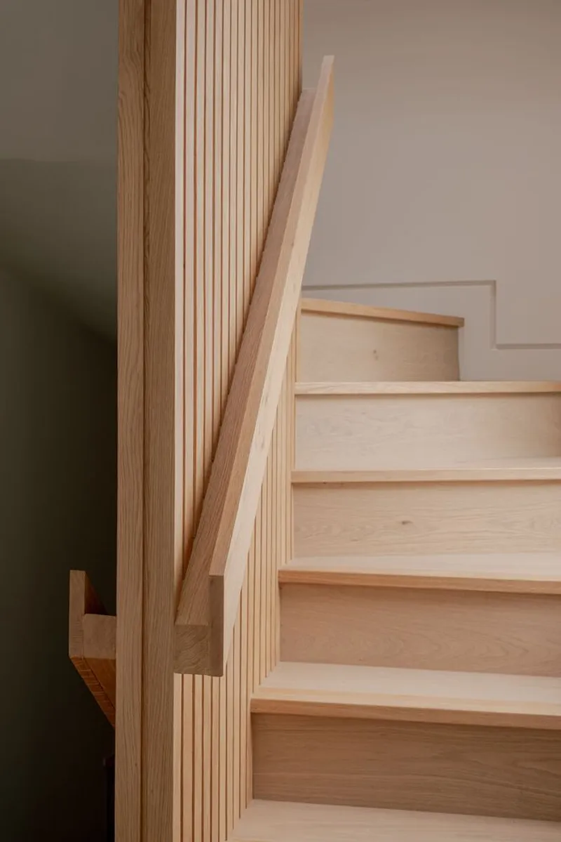 Timber staircase with fluted newel post and integrated handrail against a white wall