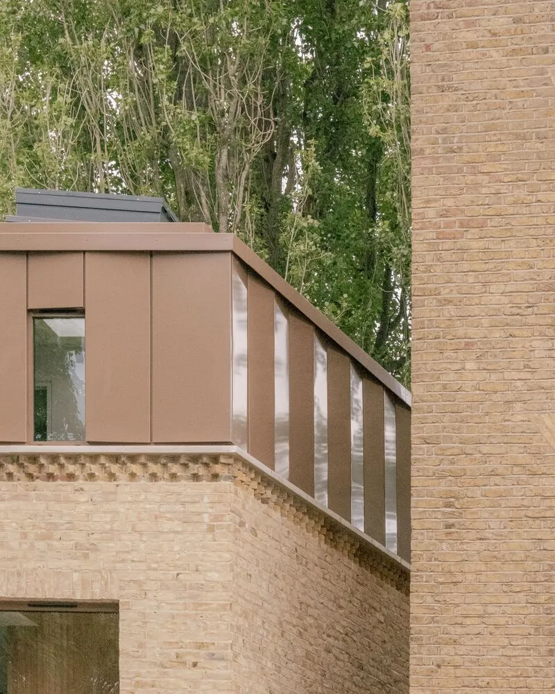 Angled metal cladding panel and brick wall junction beneath overhanging trees in daylight